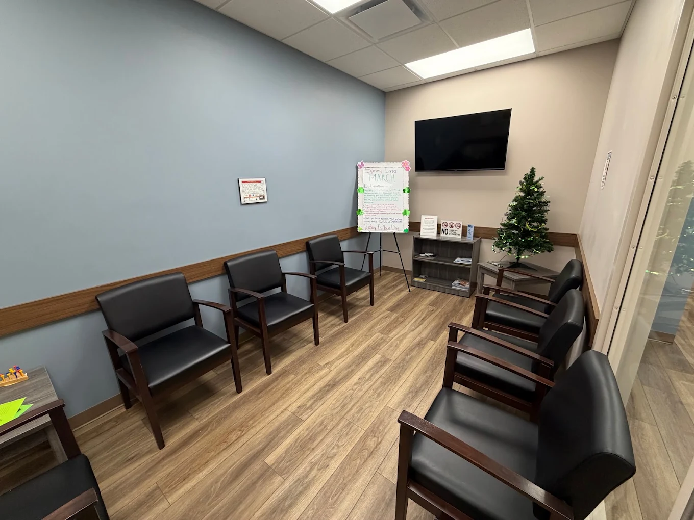 BrightView Health group room with black armchairs arranged around the walls, television, informational display, shelving, and wood-look flooring