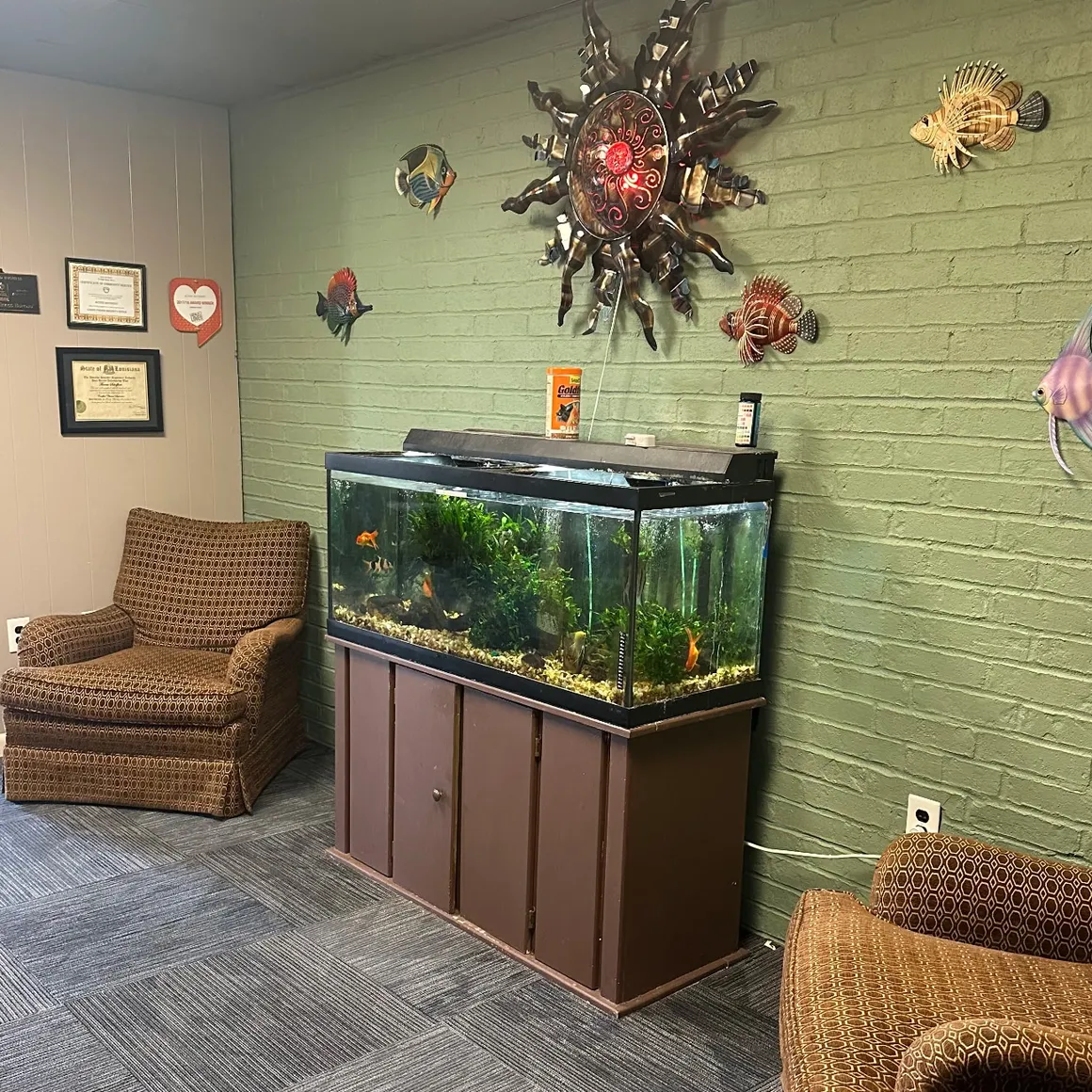 Waiting area with armchairs and large fish tank on green brick wall