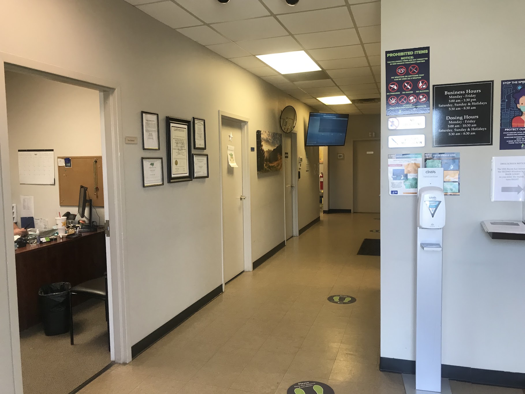 Clinic hallway with signage, certificates, and hand sanitizer stand
