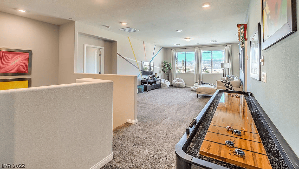Spacious upstairs recreation area with shuffleboard table, television, lounge seating, and large windows
