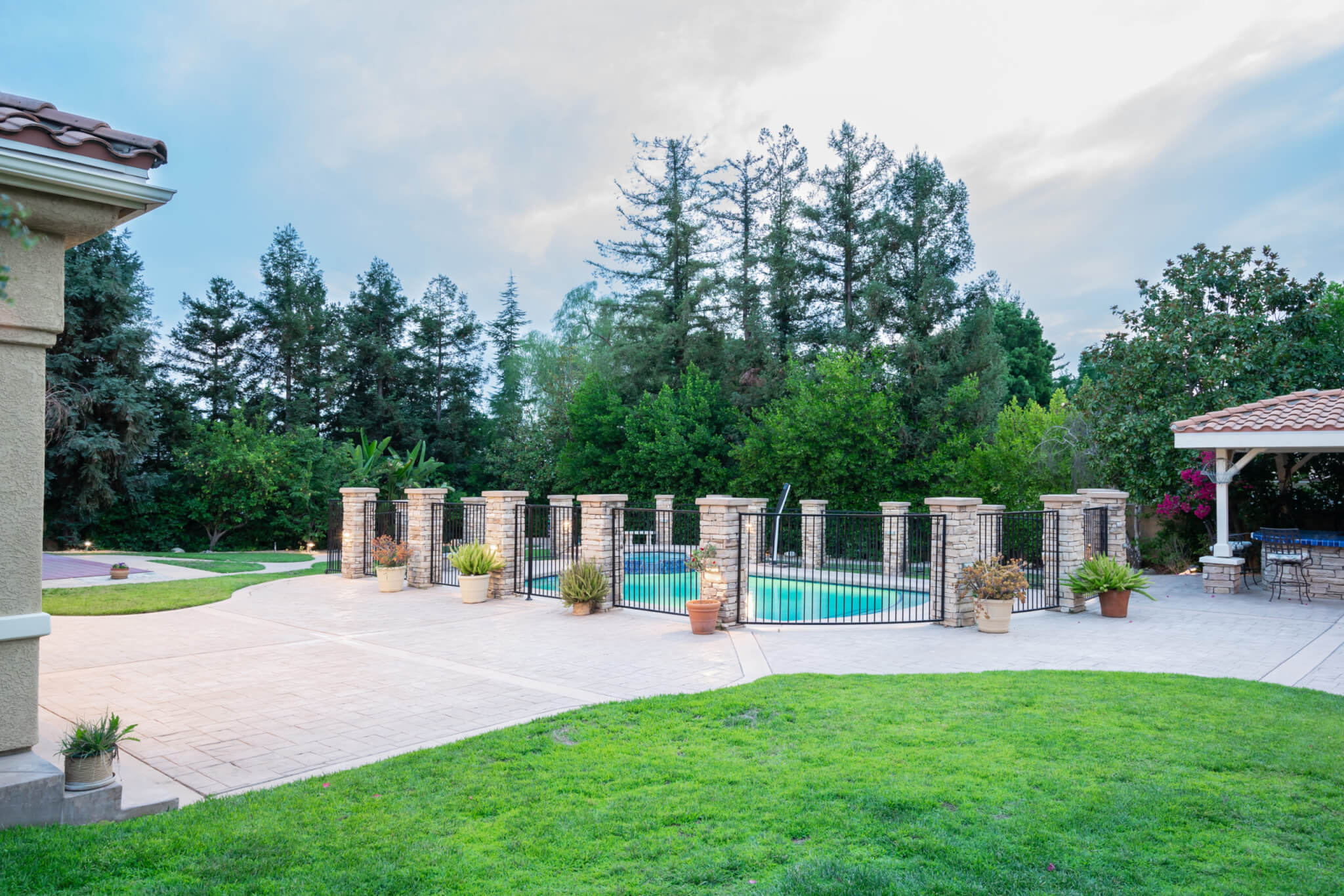 Paved patio and fenced pool area bordered by tall trees