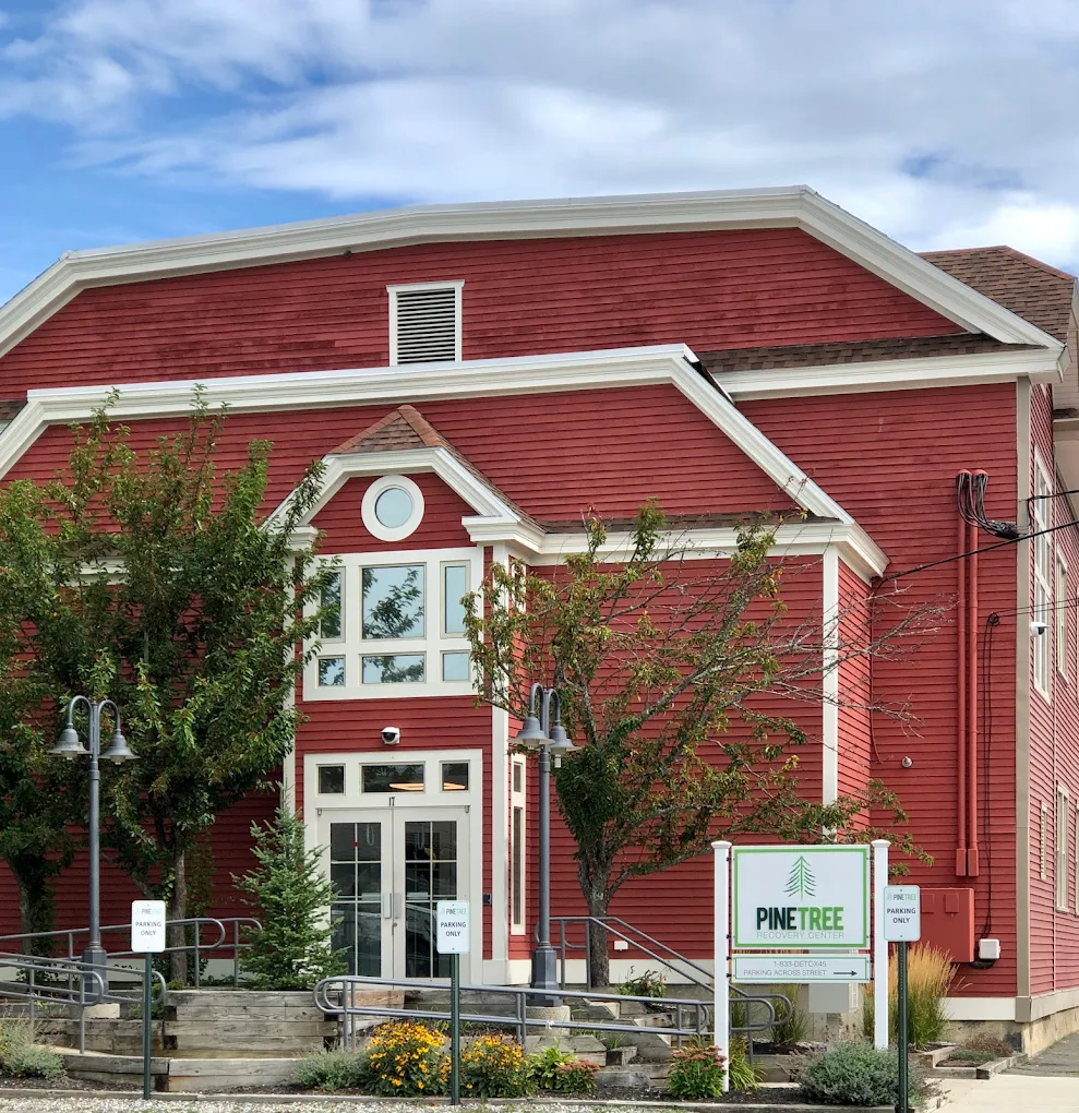 Exterior of Pine Tree Recovery Center with red siding, white trim, trees, and a welcoming sign near the entrance