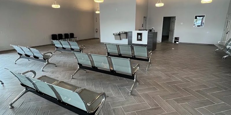 A spacious, modern waiting area with sleek metal seating, stylish hanging lights, and an open industrial ceiling, creating a welcoming environment.