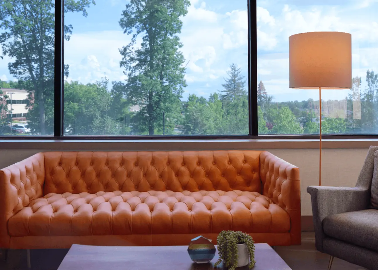 Bright lounge with orange tufted sofa and large window