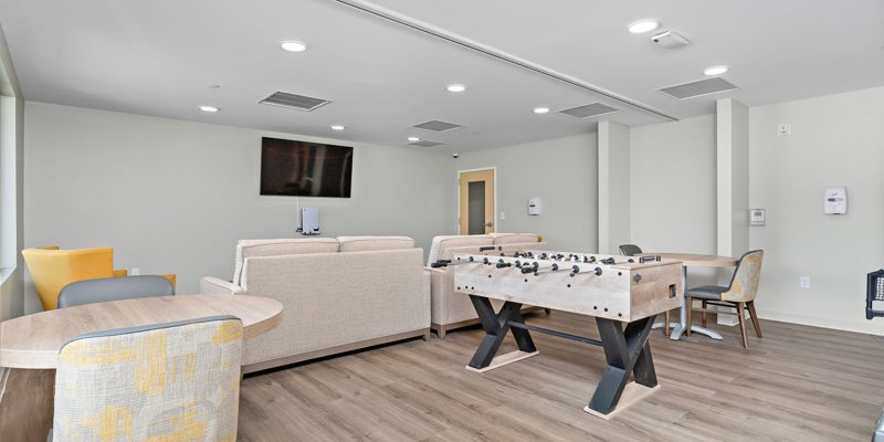  A recreational room featuring comfortable seating, a foosball table, a wall-mounted TV, and bright decor. The space feels fun, modern, and inviting.