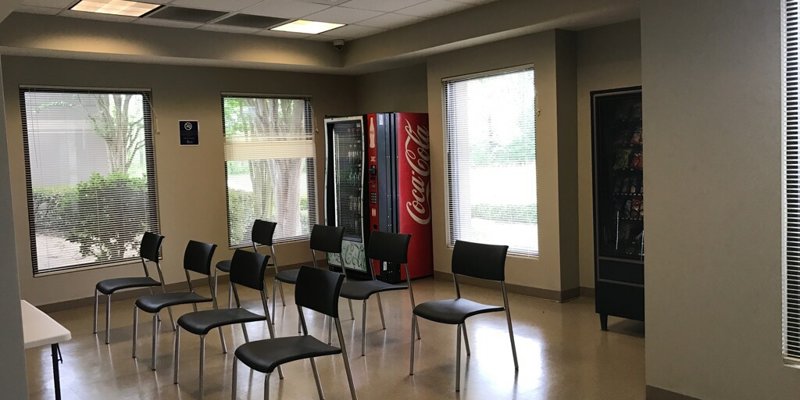  A simple break room with chairs arranged in rows, vending machines, and large windows providing natural light, offering a calm and relaxed atmosphere.