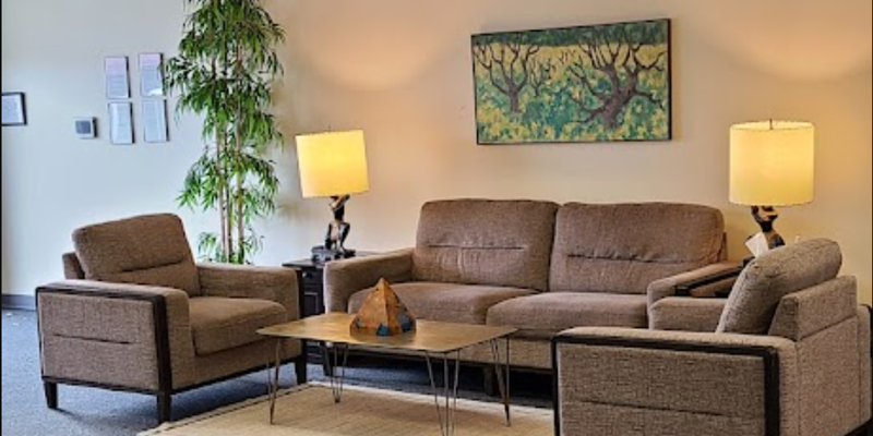  A cozy seating area featuring comfortable brown sofas, warm lighting, and a large plant. Art on the wall adds to the peaceful ambiance.