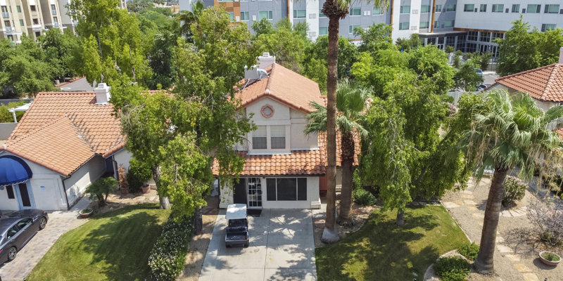 Charming two-story house with a red tile roof, surrounded by lush greenery and palm trees, offering a peaceful and inviting atmosphere.