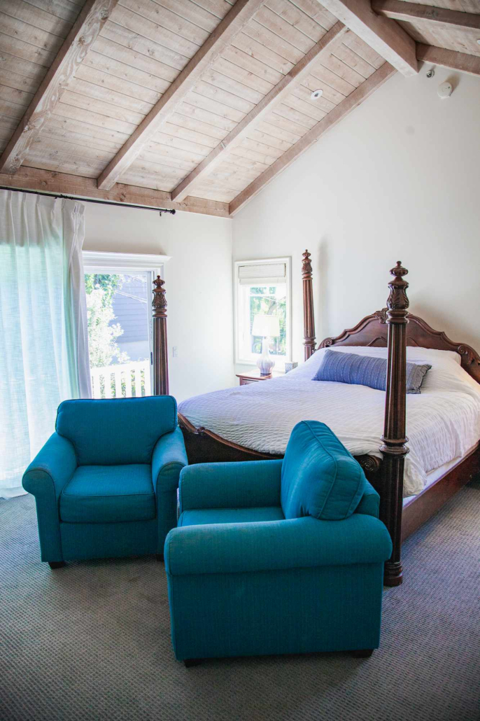 Large bedroom with wood-beam ceiling, king bed, and two blue chairs.