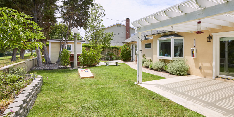  Beautiful backyard with lush green grass, cozy seating, a cornhole game setup, and a shaded pergola, perfect for relaxation and outdoor fun.