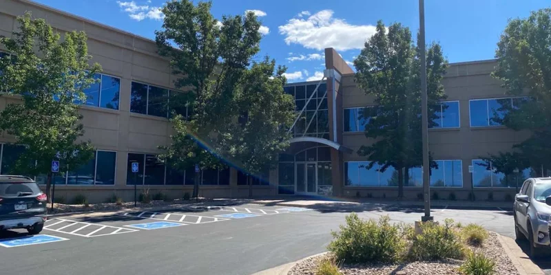 A modern, two-story building with large glass windows and surrounded by trees. Accessible parking spaces are available in the front.