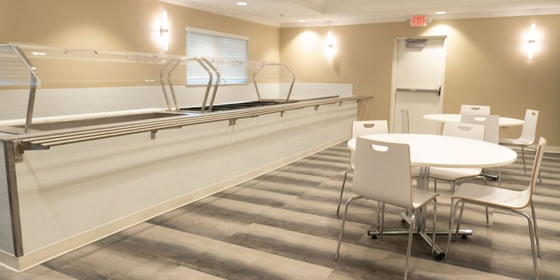 A clean and modern dining area with light wood floors, sleek white tables, and chairs, ready for meals or gatherings in a welcoming space.