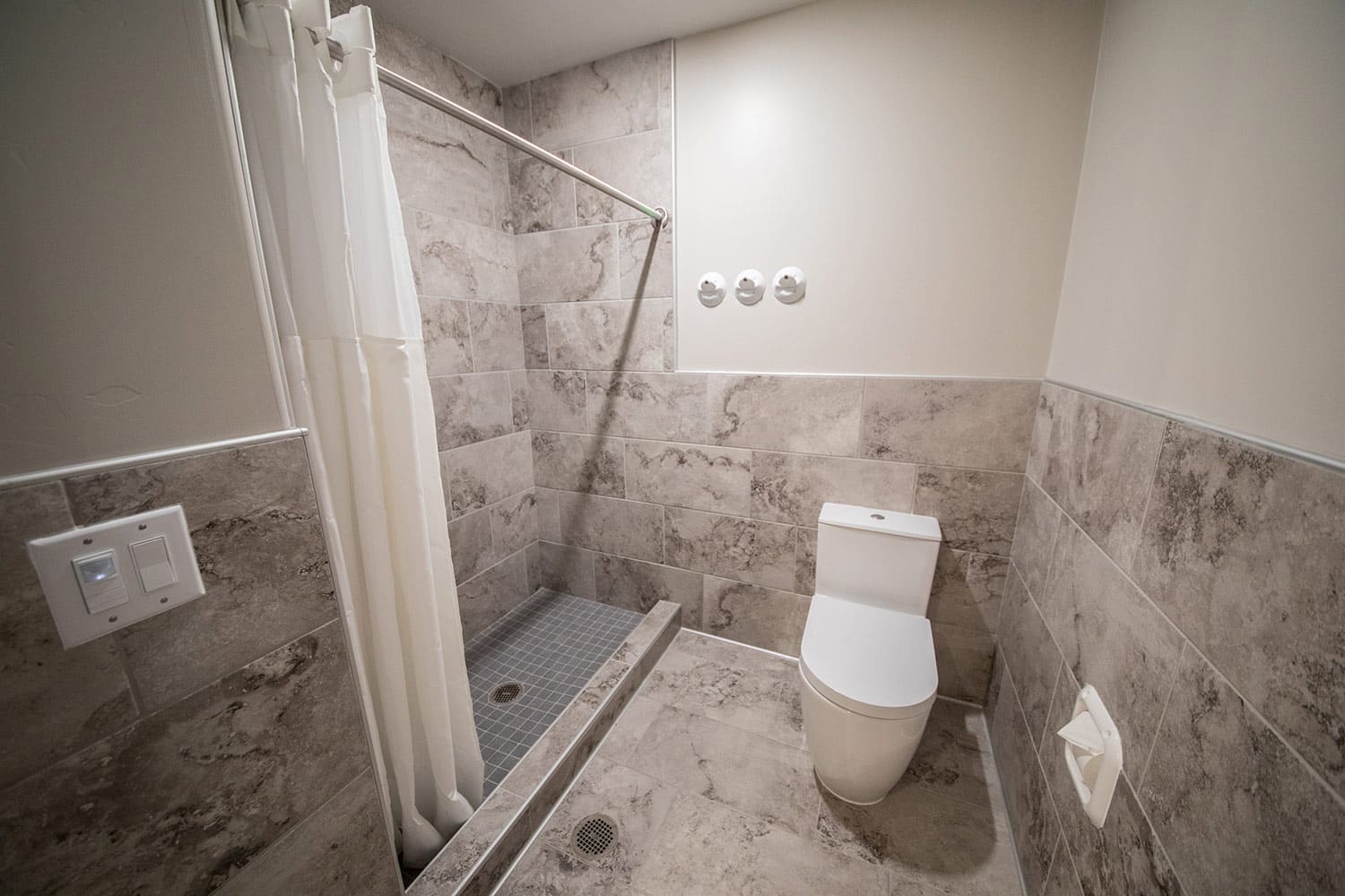 Shared bathroom with walk-in shower, tile walls, and toilet