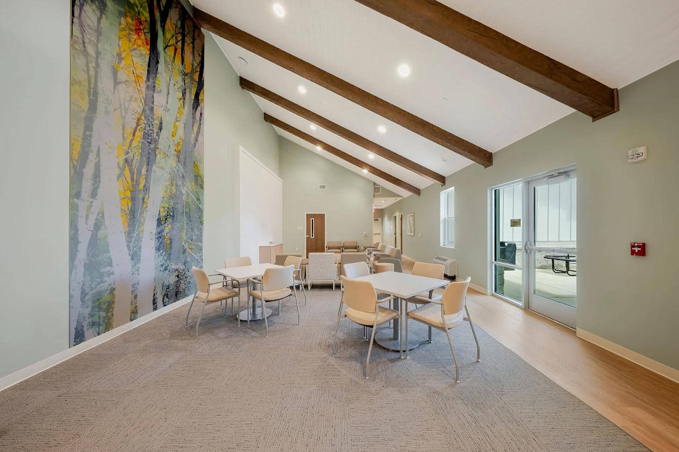 Large community and dining room with multiple tables, chairs, pendant lights, and exposed wood ceiling beams