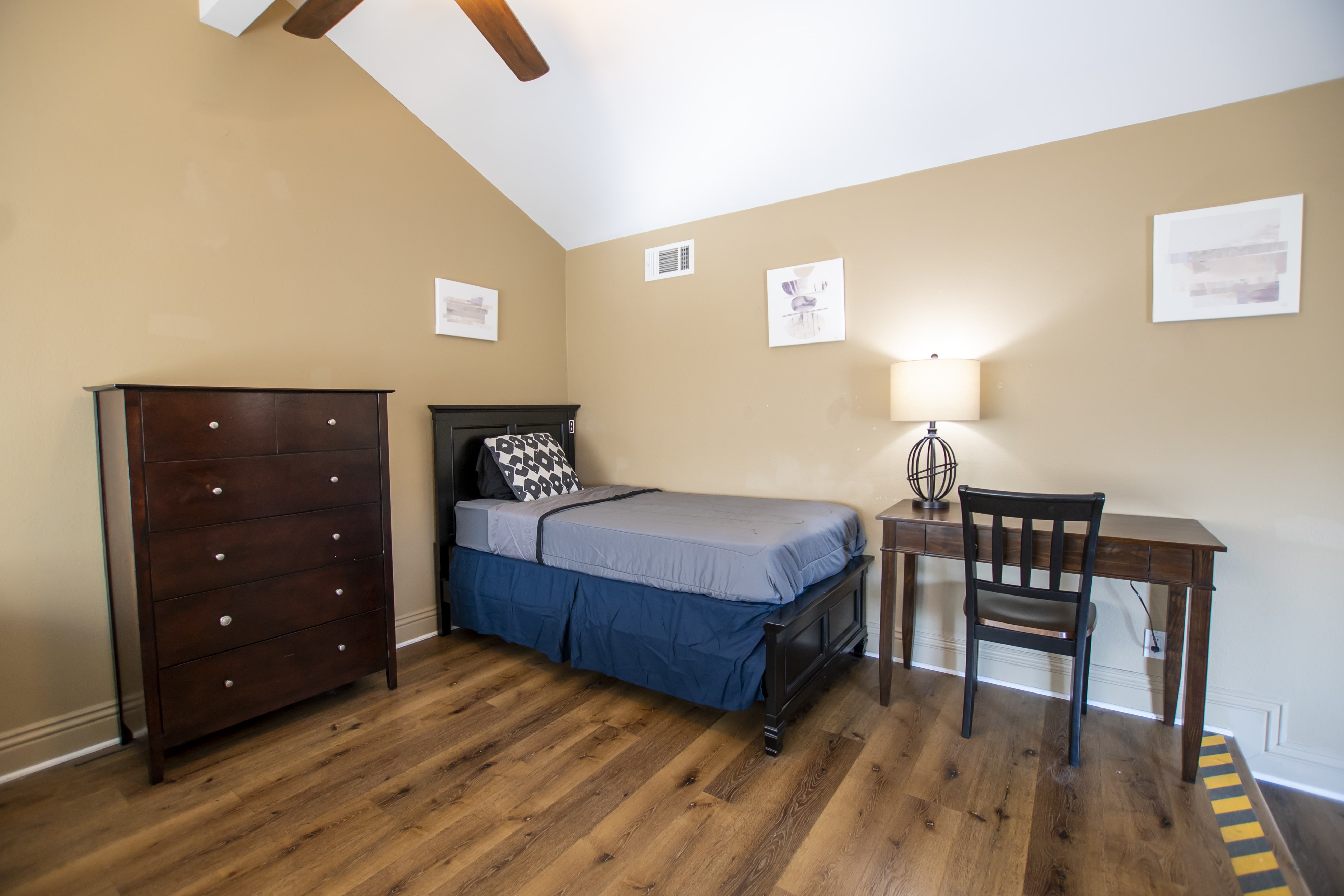 Neatly made bed with a desk and dresser