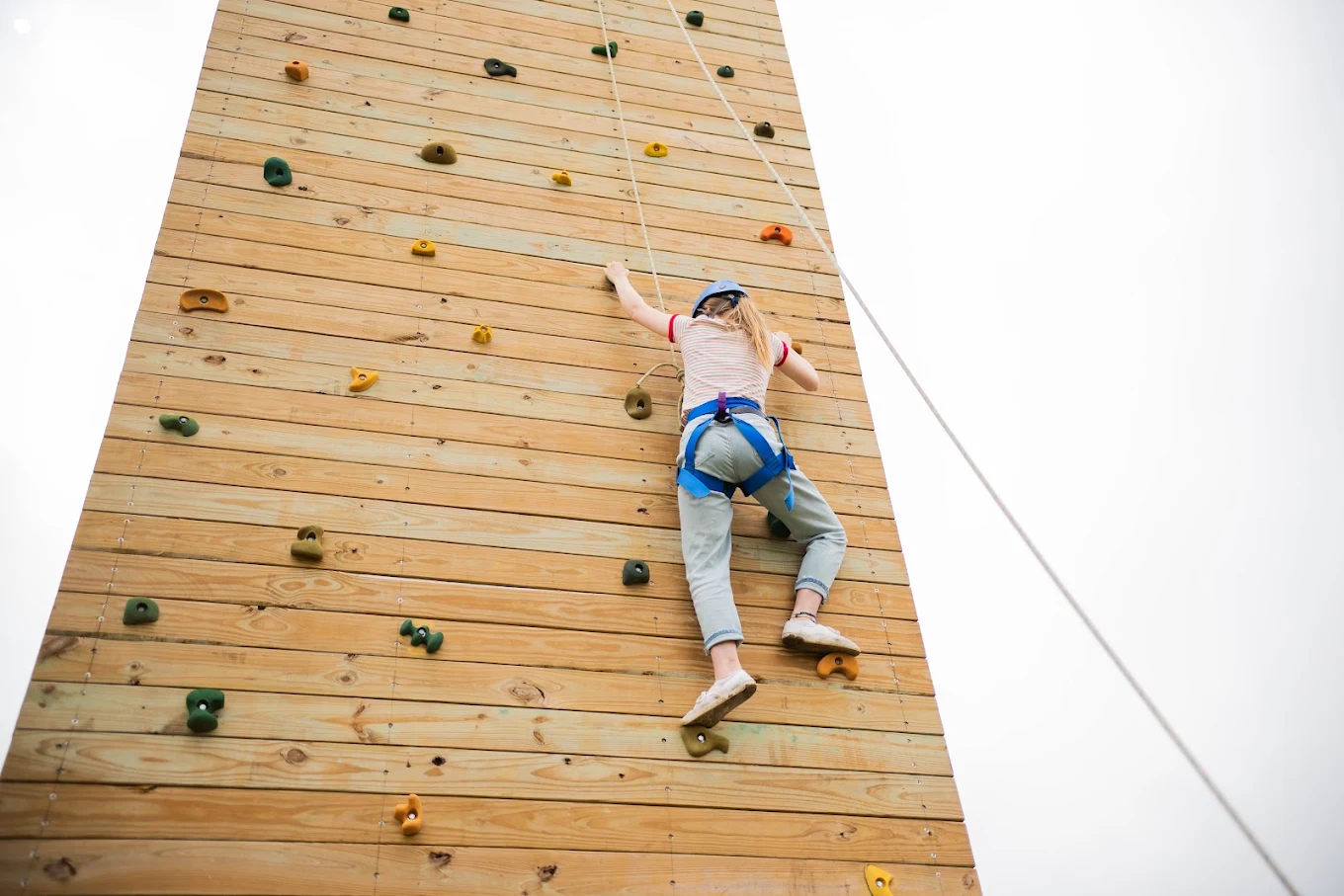 Person climbing an outdoor rock wall with a safety harness