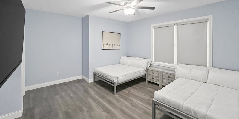 Simple, serene bedroom with two neatly made beds, soft lighting, and calming decor, offering a peaceful and comfortable environment.