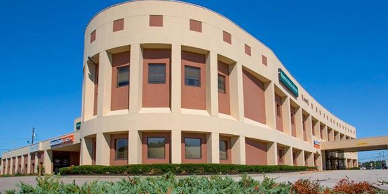 A modern, curved building with large windows and a clean facade, surrounded by well-maintained landscaping under a bright blue sky.