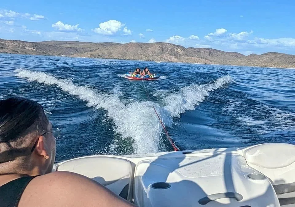 People enjoying tubing behind a boat on a lake with desert mountains in the background