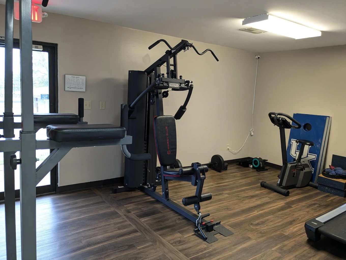Fitness room with multi-function gym equipment, stationary bike, dumbbells, and wood-style flooring