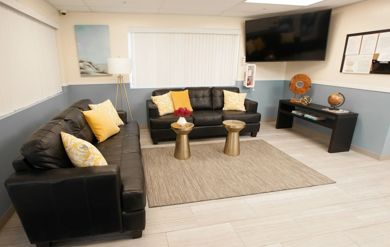 Lounge with black sofas, yellow pillows, and wall-mounted TV