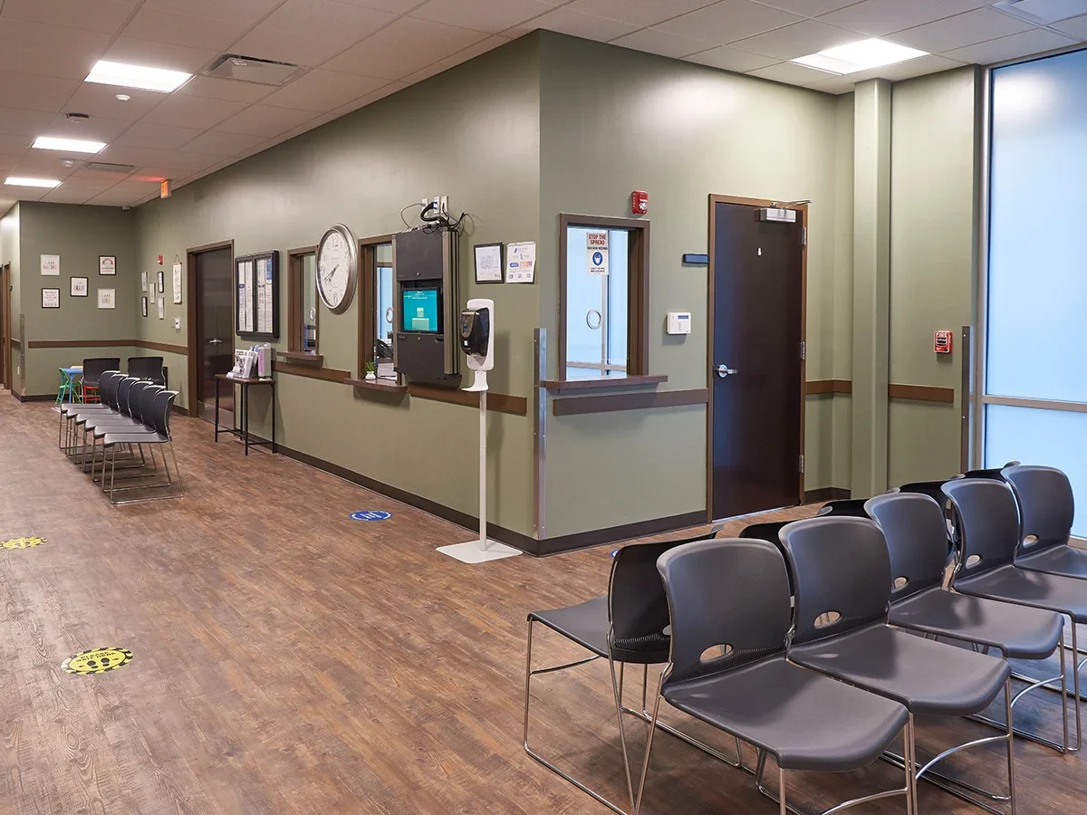 Wide hallway with rows of chairs, reception window, and wall clock