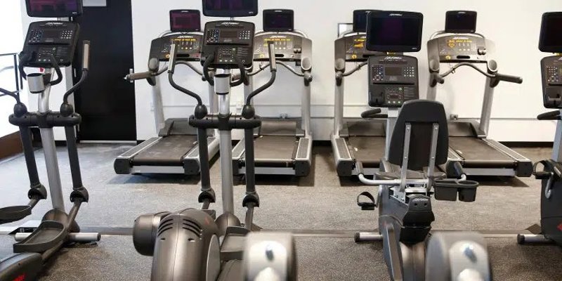 A well-equipped fitness room features multiple treadmills, ellipticals, and other cardio machines, offering a clean, modern space for exercise.