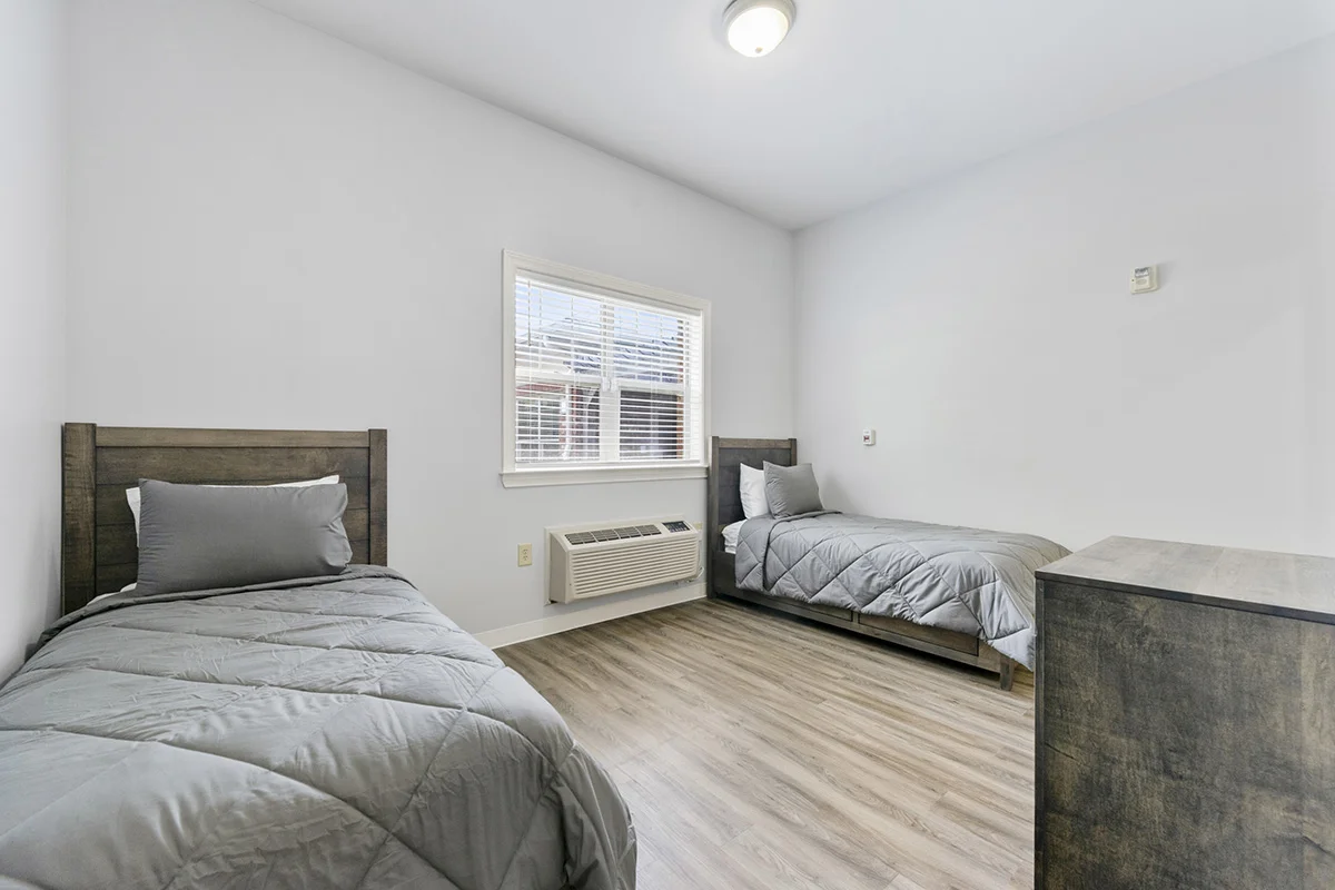Shared resident bedroom with two twin beds, dresser, air conditioning, and natural light