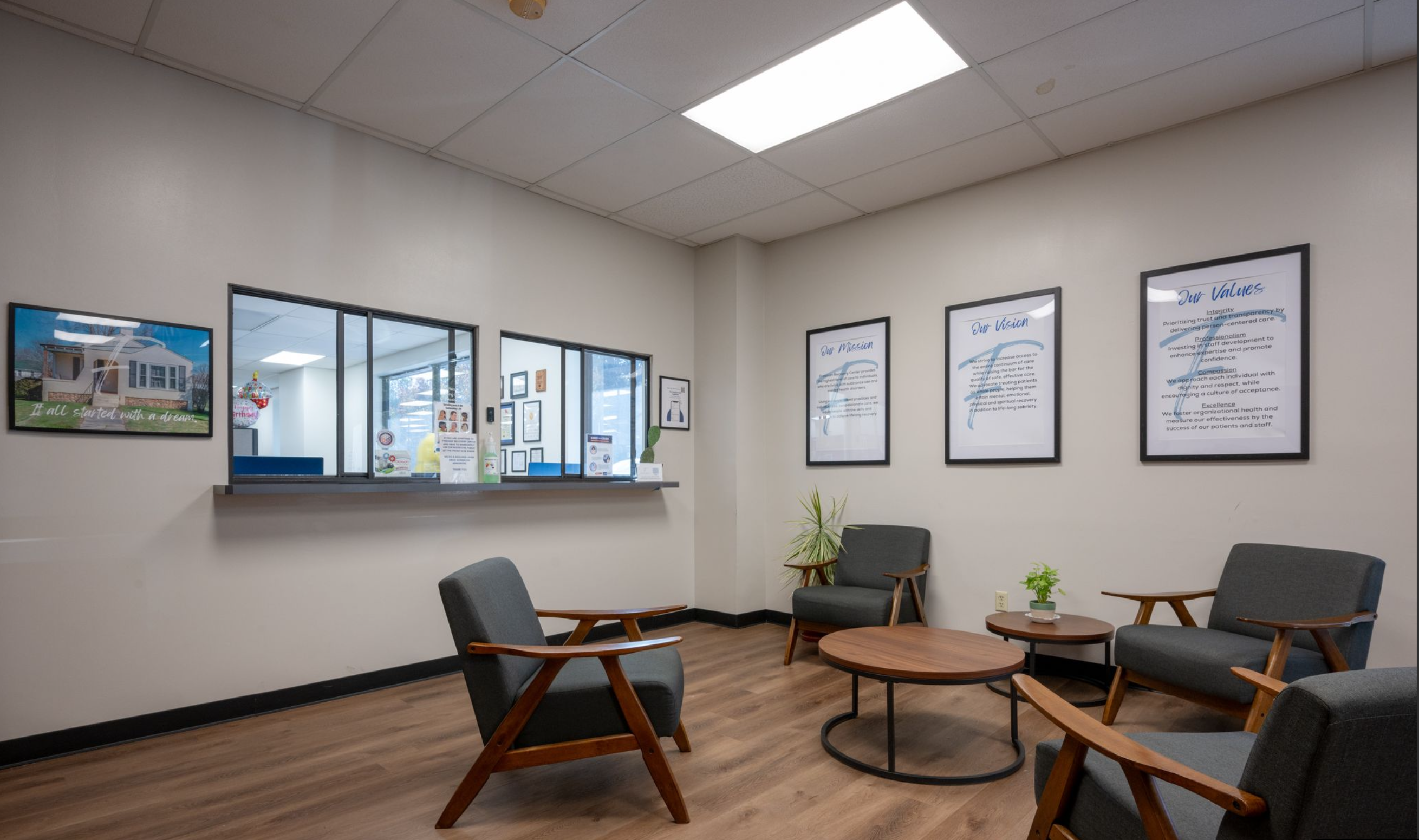 Spacious waiting area with modern chairs, reception window, and plants