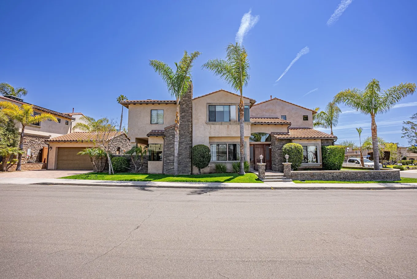 Two-story recovery residence with palm trees and stone accents