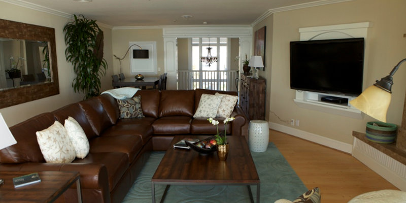 A cozy living room features a large leather sectional, stylish decor, warm lighting, and a mounted TV, creating a comfortable, inviting space.