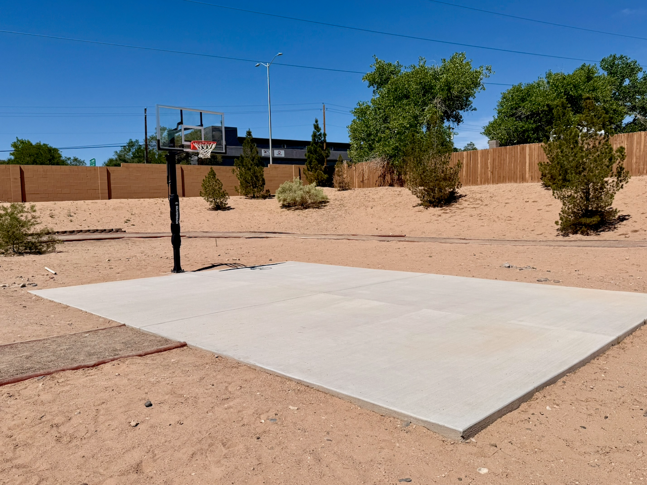 Outdoor basketball half court surrounded by desert landscaping and a fenced property boundary
