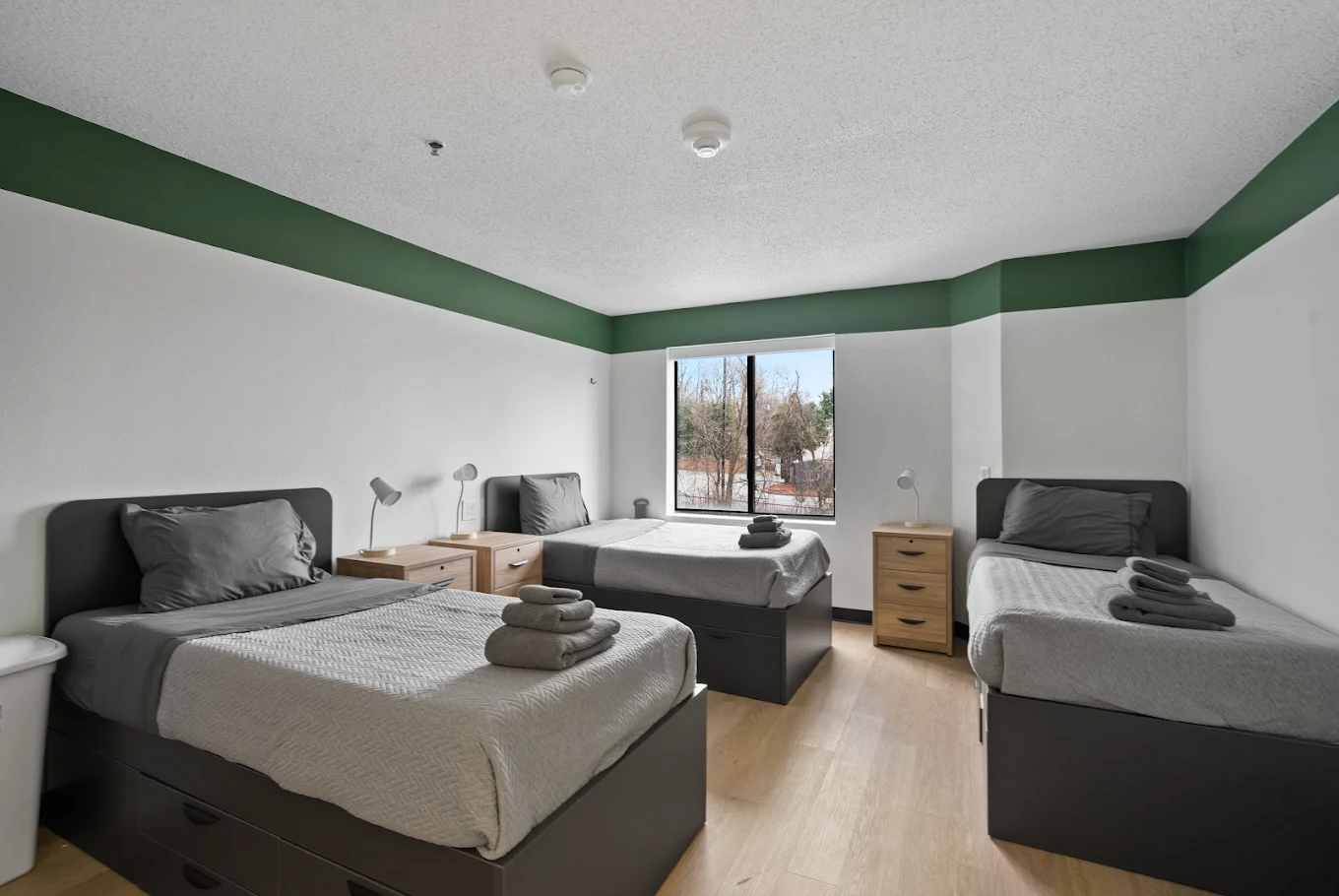 Triple twin-bed room with natural light, wood floors, and simple furnishings