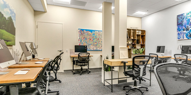  A well-lit workspace with multiple computer stations, ergonomic chairs, and bright artwork on the walls, creating a productive and inviting atmosphere.