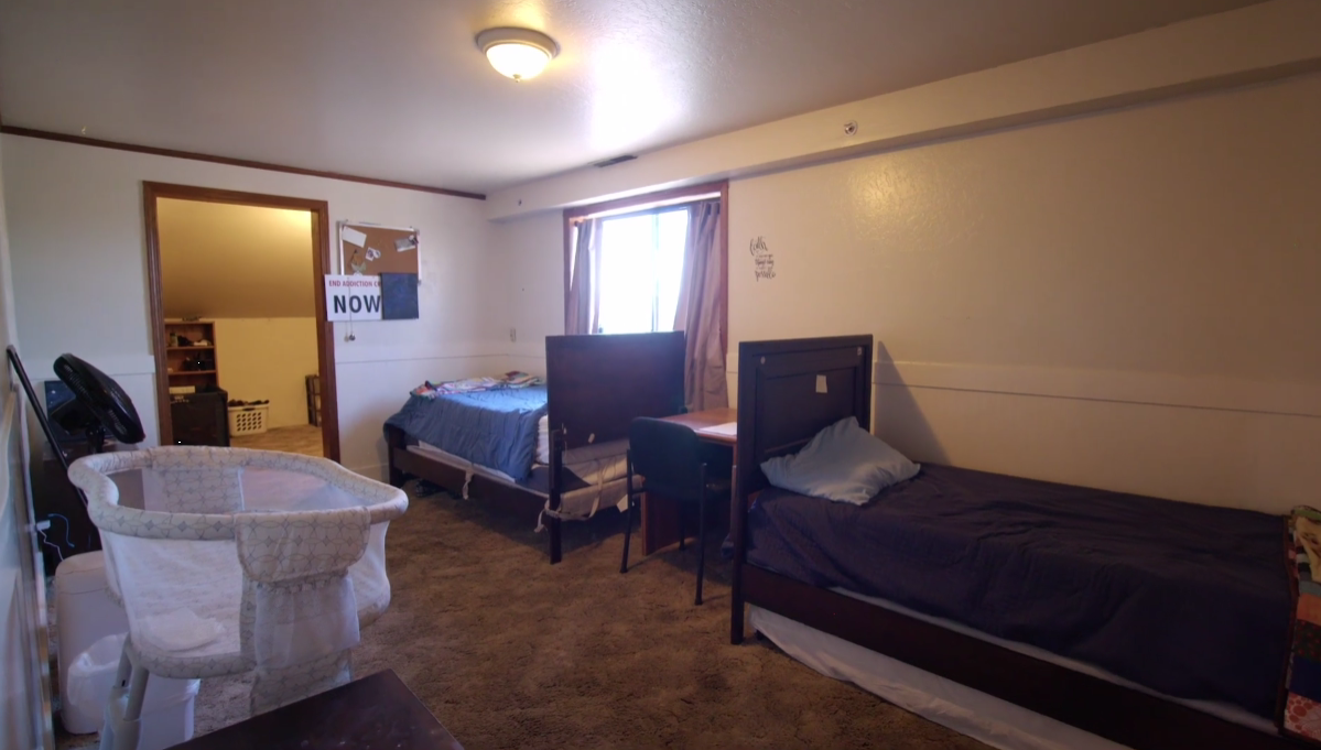 Bedroom with two twin beds, a crib, and a desk near window