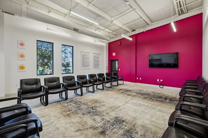 A group therapy room with an accent pink wall and several chairs.