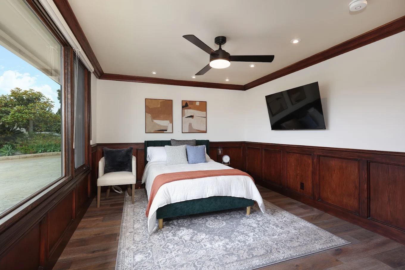 Private bedroom with queen bed, wood-paneled walls, large window, and wall-mounted TV