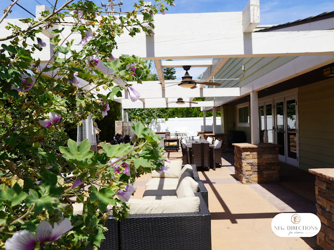Covered patio with seating and dining area beside flowers