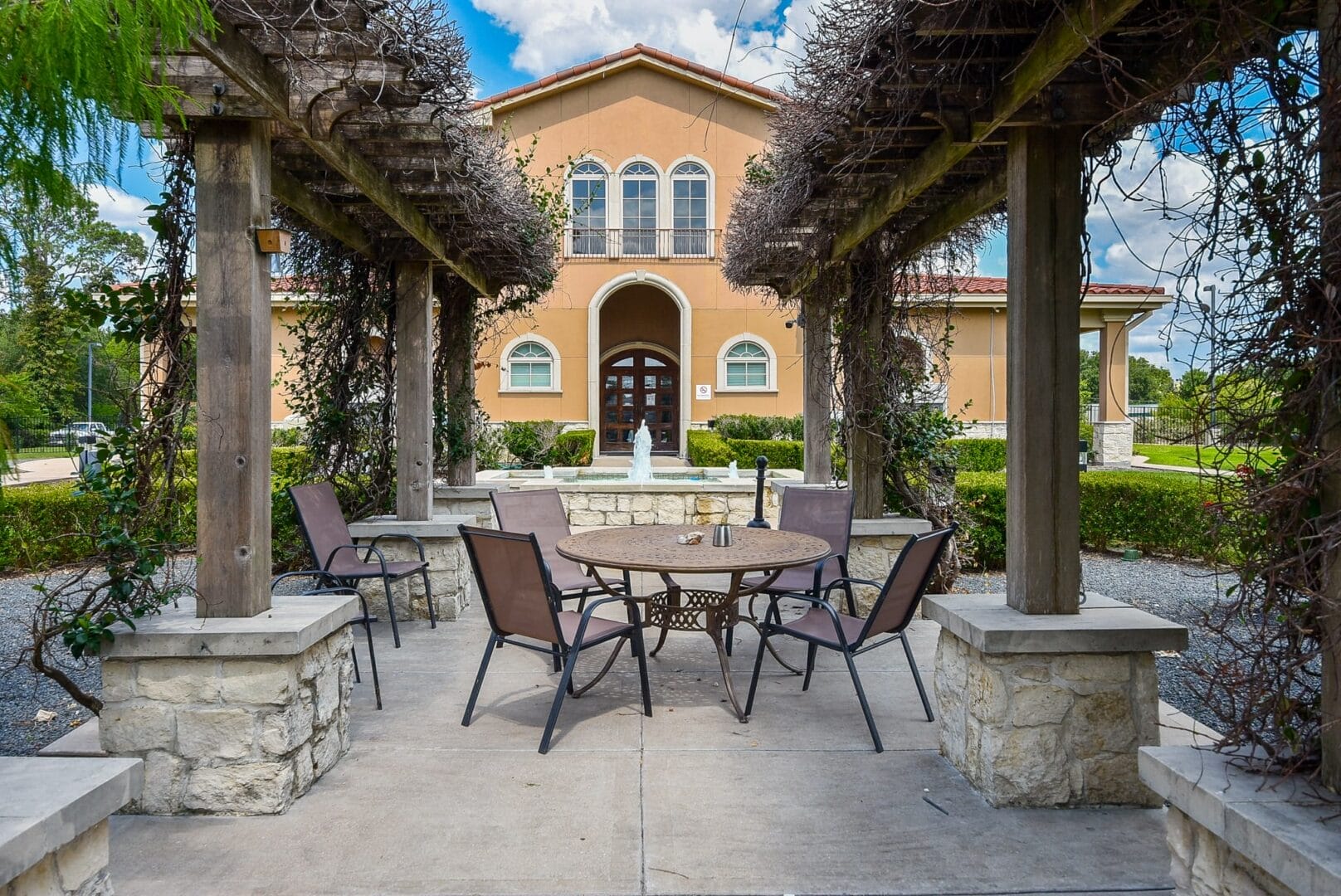 a wooden pergola, surrounded by greenery, and a fountain.