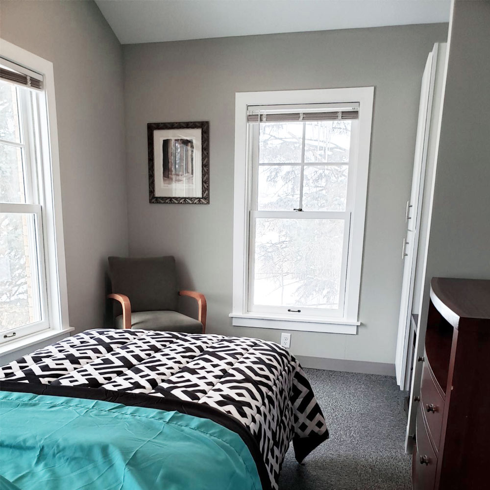 Single bed near windows with teal bedding and wood furniture