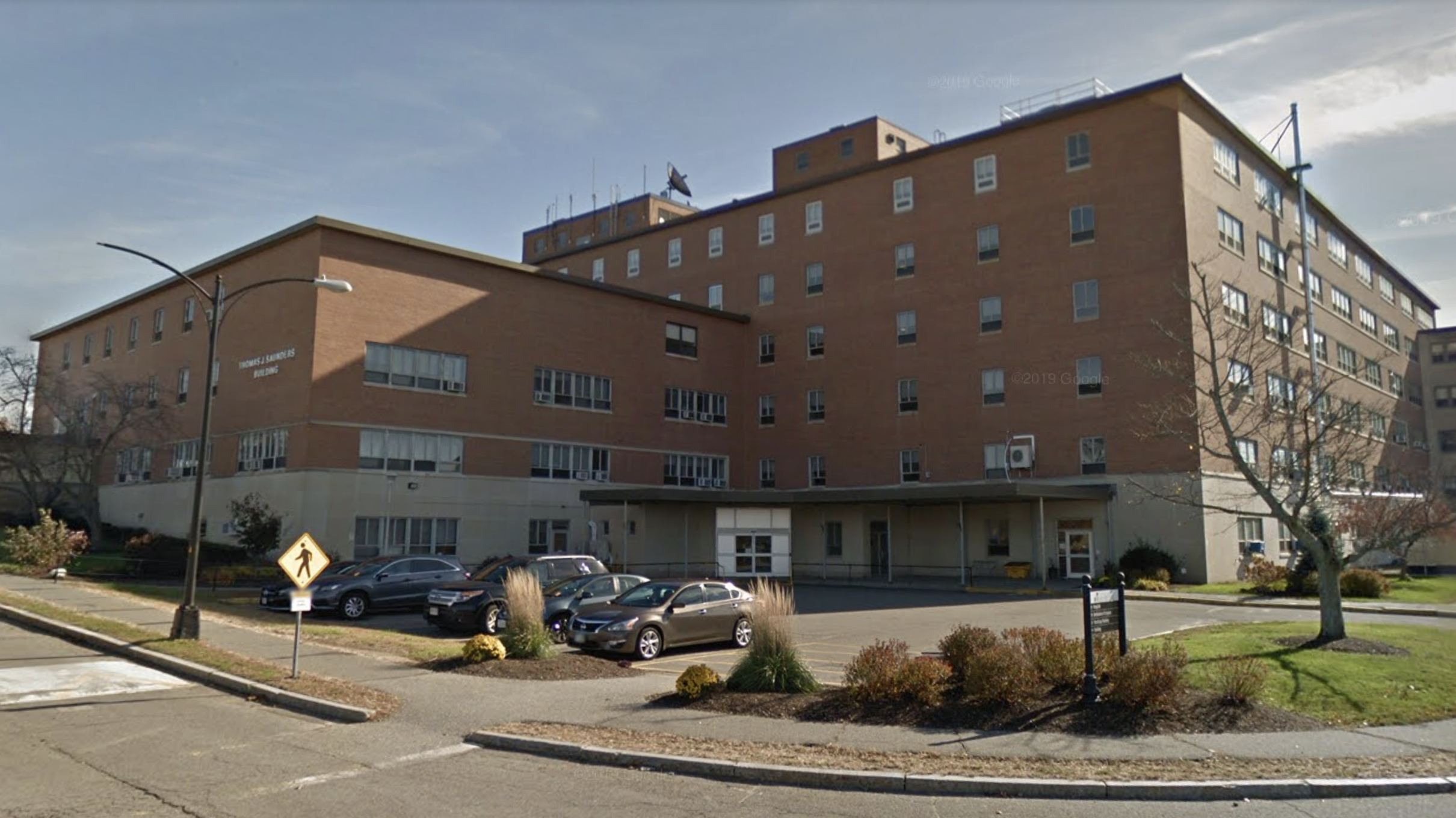 Large multi-story brick building with parking area and trees