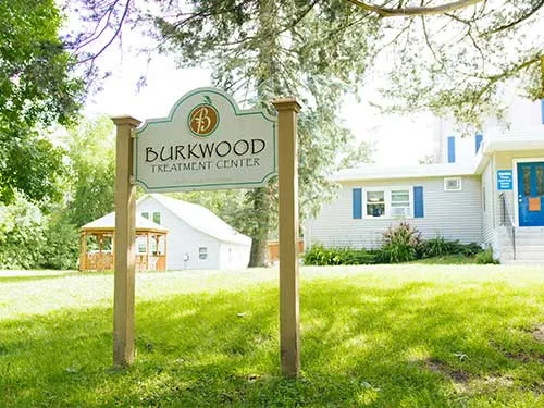 Facility sign in grassy front yard under shaded trees