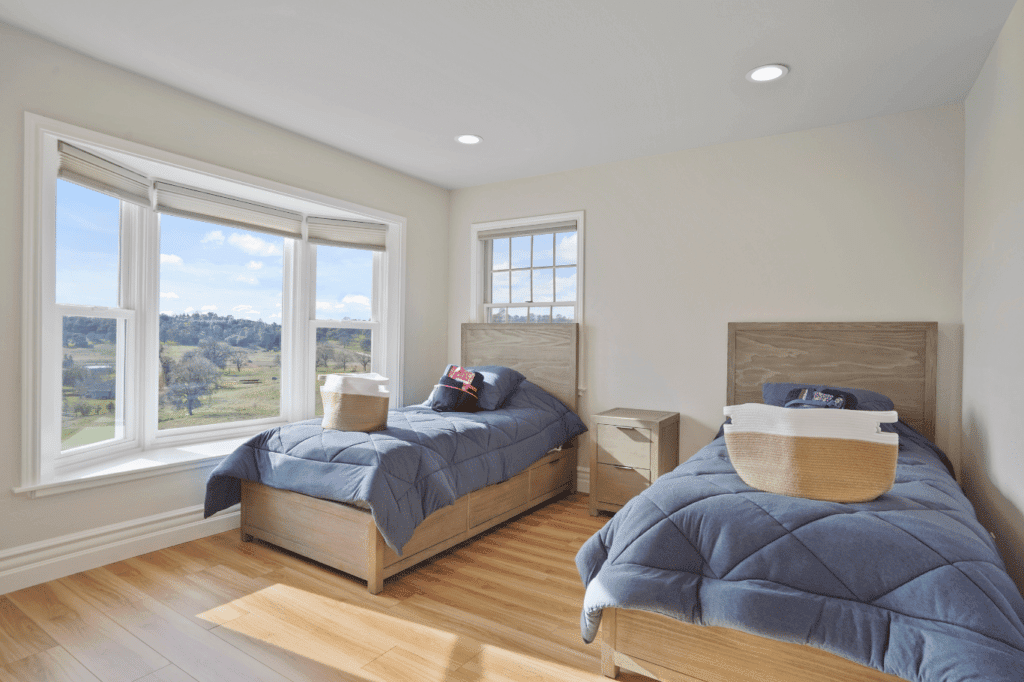 Bright shared bedroom with two twin beds and large window overlooking hills.