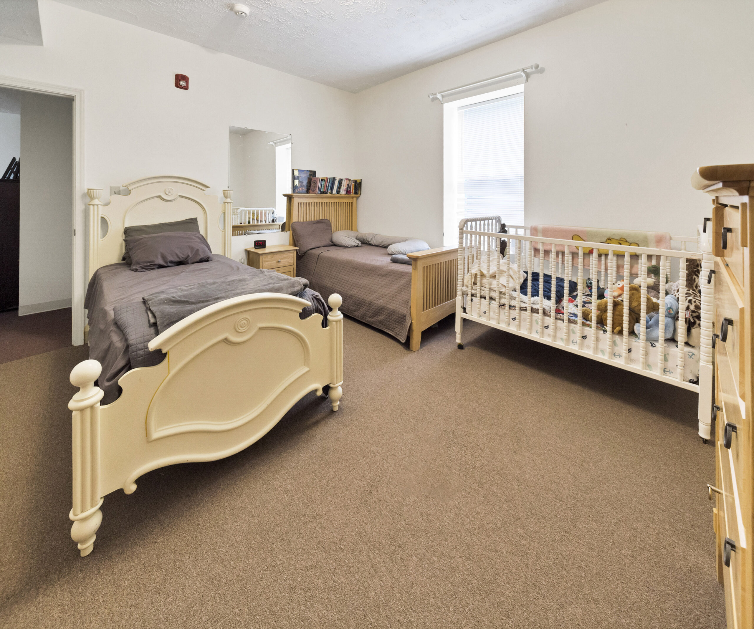Shared bedroom with twin beds, crib, dresser, and neutral decor