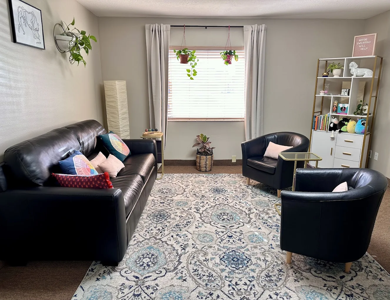 Private therapy space with black leather couch, chairs, bookshelves, and decor plants in a softly lit room at New Roads Behavioral Health