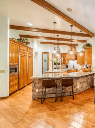 Residential-style kitchen with wood cabinetry, stone breakfast bar, and pendant lighting
