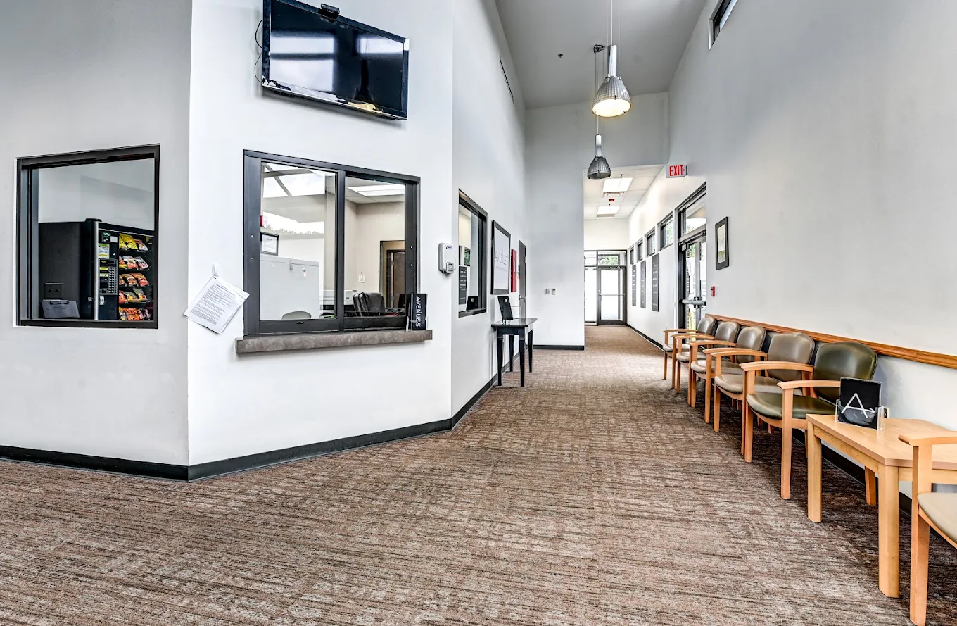 Bright facility lobby with reception windows, waiting chairs, high ceilings, pendant lights, and a wall-mounted television