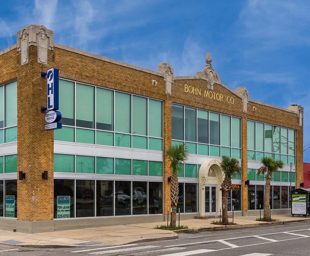 Two-story brick building with large windows and palm trees