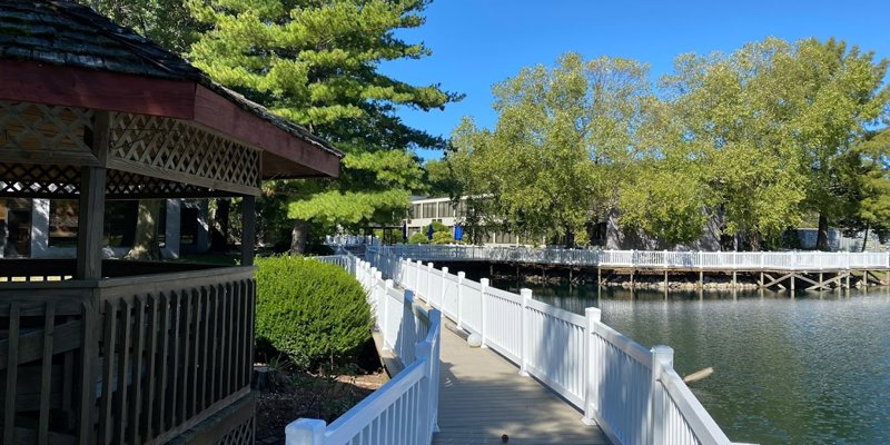 Inviting boardwalk lined with white railings, leading past a charming gazebo and serene lakeside.