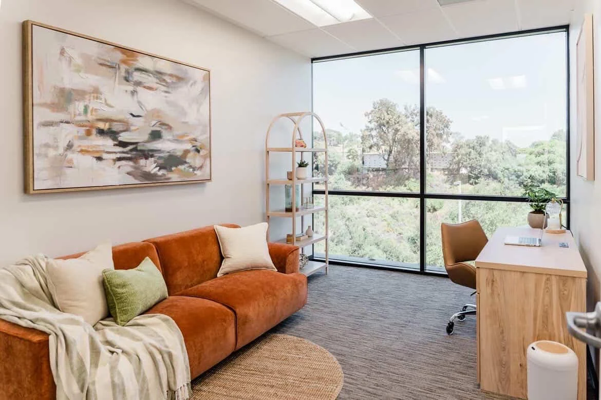 Private therapy office with sofa, desk, and large windows